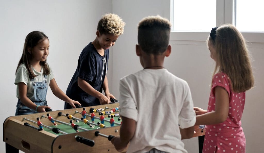 Group of multi-cultural cute children spending playtime with friends playing foosball together.