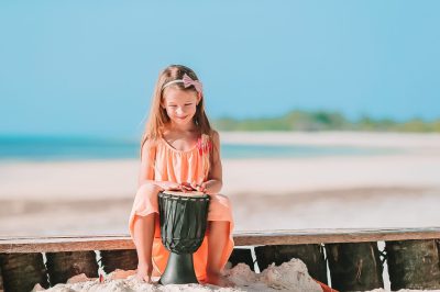 Little happy girl playing on african drums.